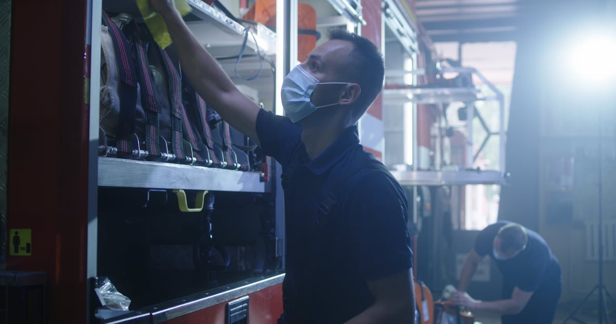 Male firefighter putting on mask and starting to wipe fire engine from dust during work on station