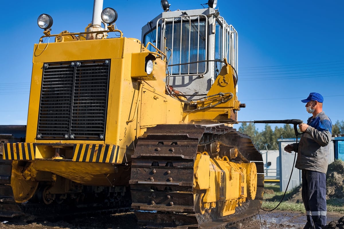 Worker pressure washing yellow construction tractor