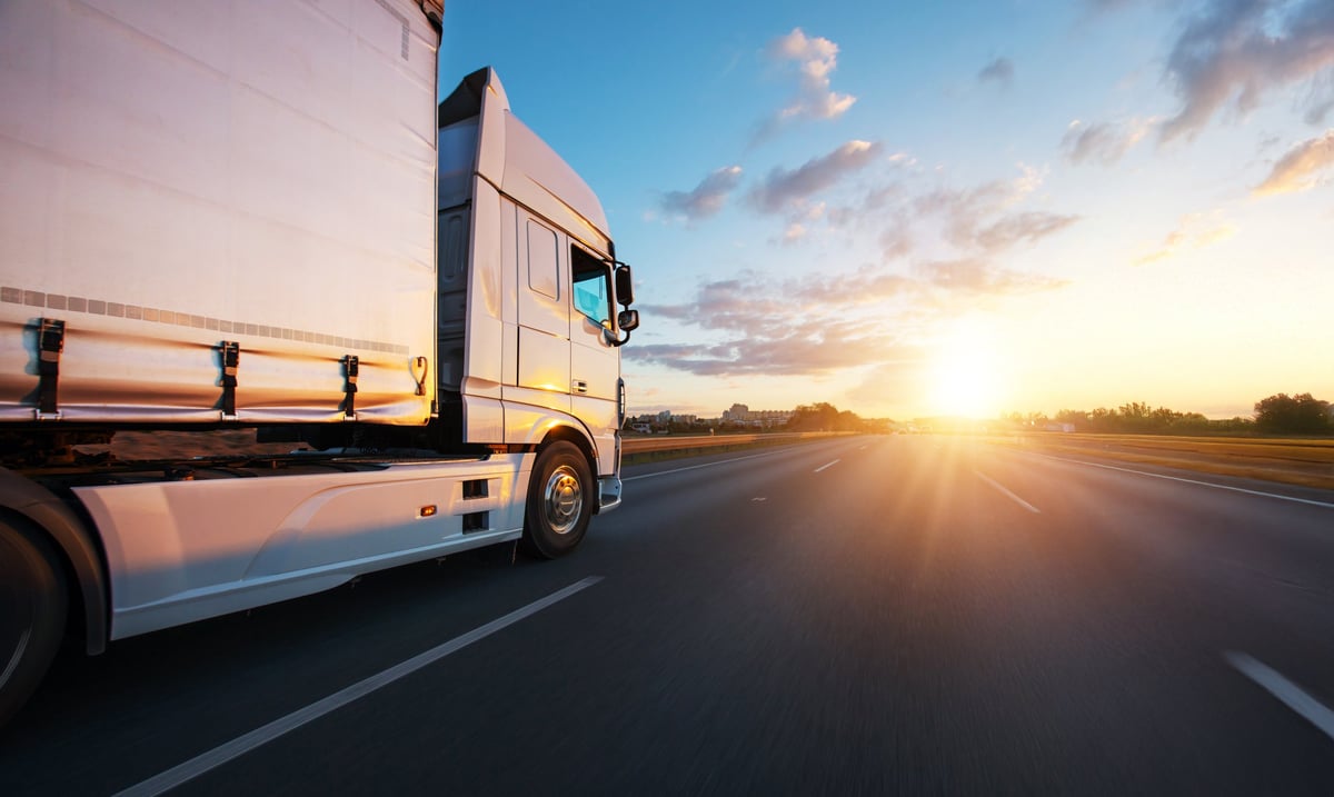 European truck driving on the asphalt road in rural landscape at sunset. Transportation and cargo concept.