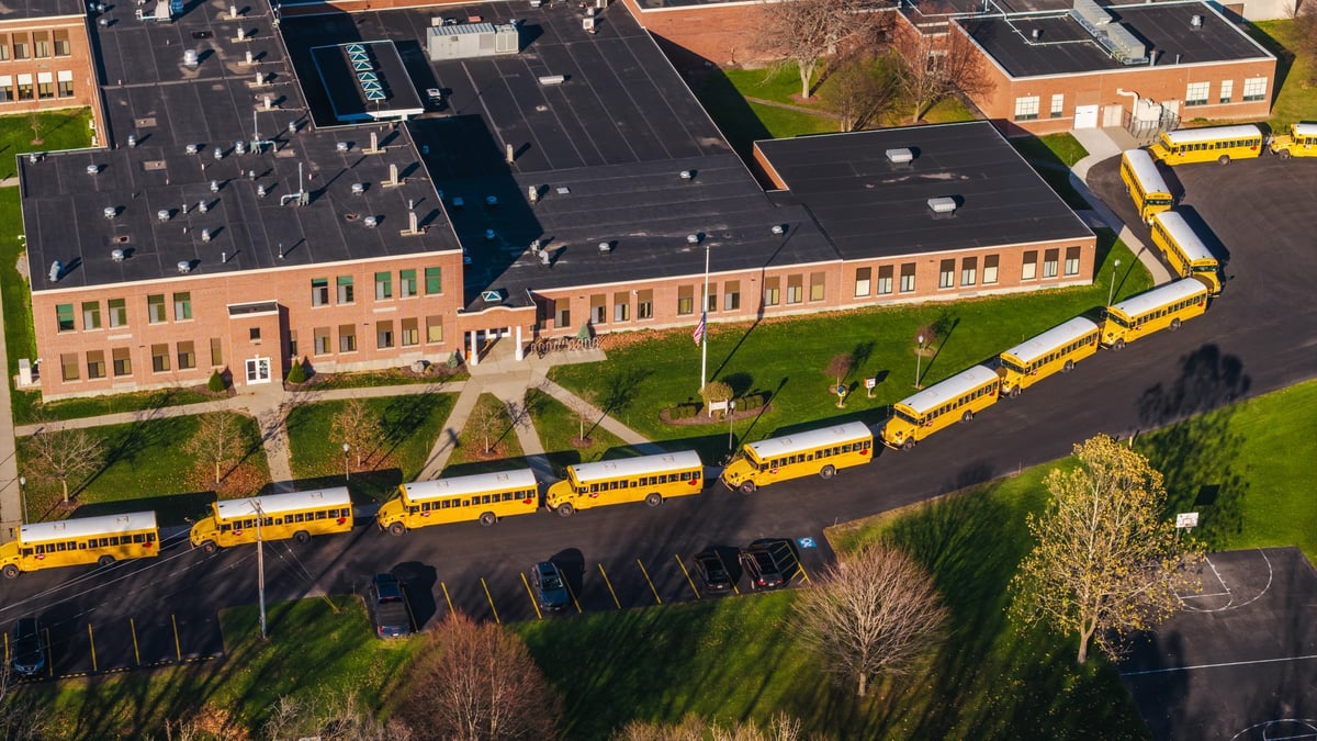 Aerial view of a typical American school with a long row of yellow school buses lined up outside the building on a sunny autumn day