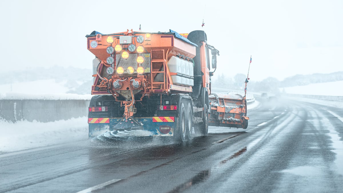 Snow plow sprinkles highway with road salt in freezing weather.