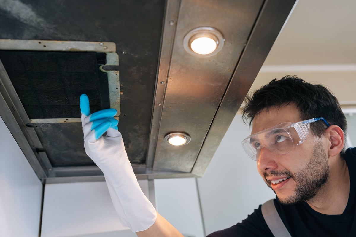 Professional male worker with safety glasses and gloves performing inspection on dirty kitchen range hood filter