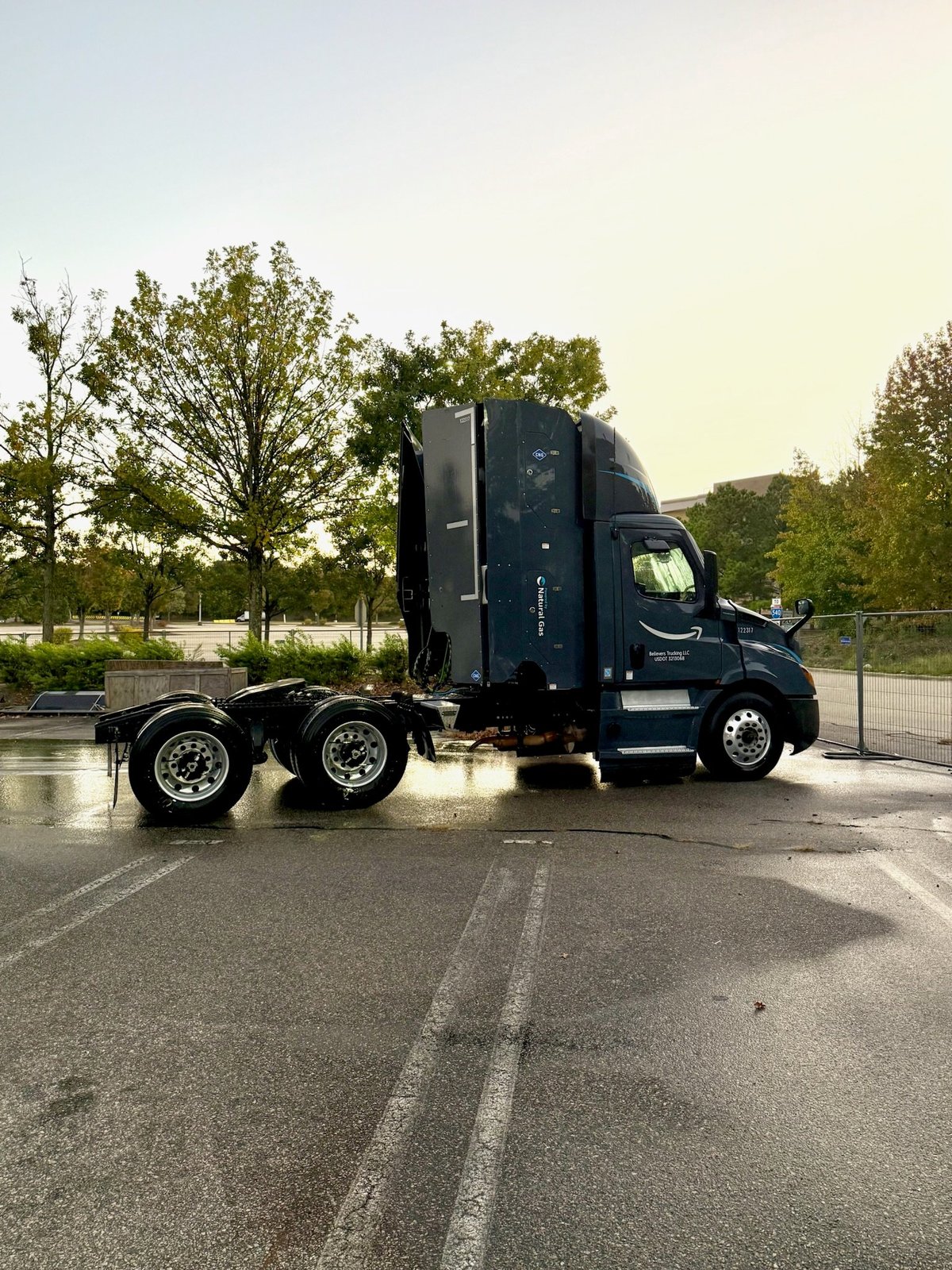 Dark blue semi-truck parked on wet asphalt with trees in background