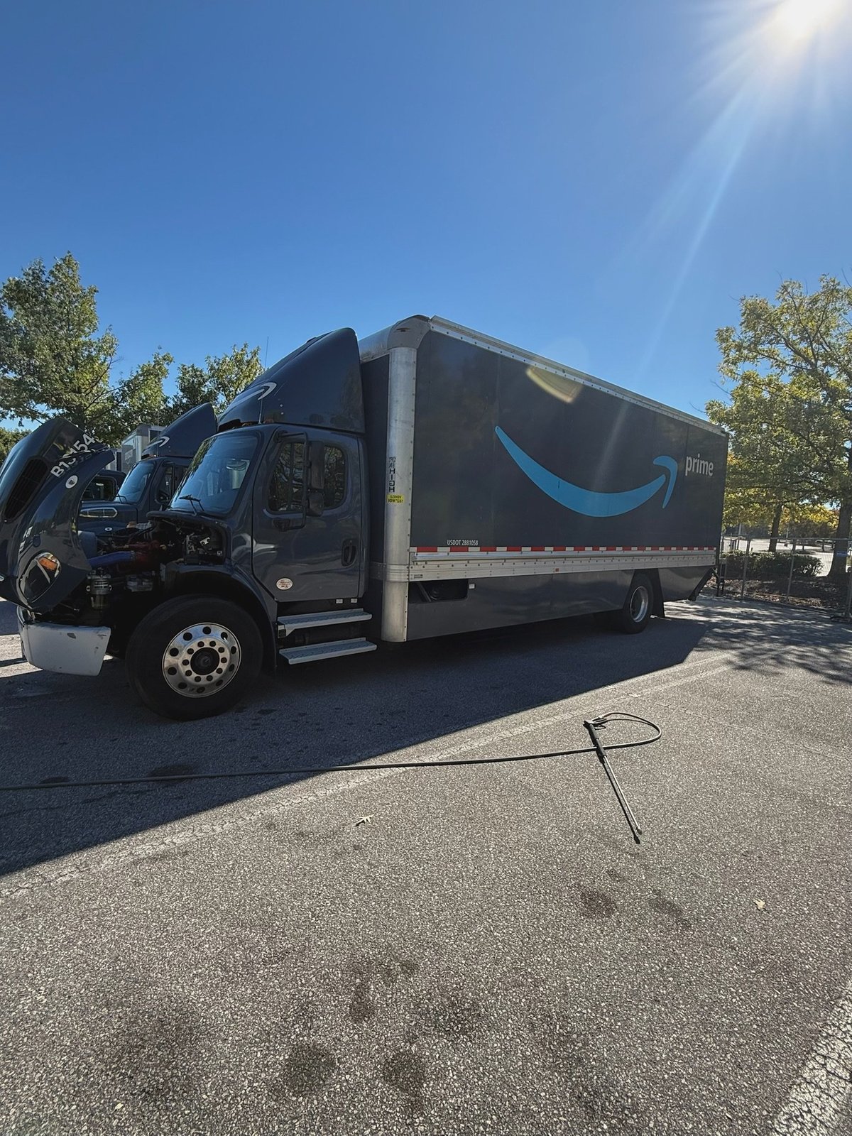 Amazon delivery truck parked on asphalt lot under sunny blue sky with trees in background