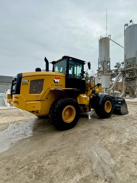 Yellow heavy equipment wheel loader parked on dirt ground with industrial silos in background