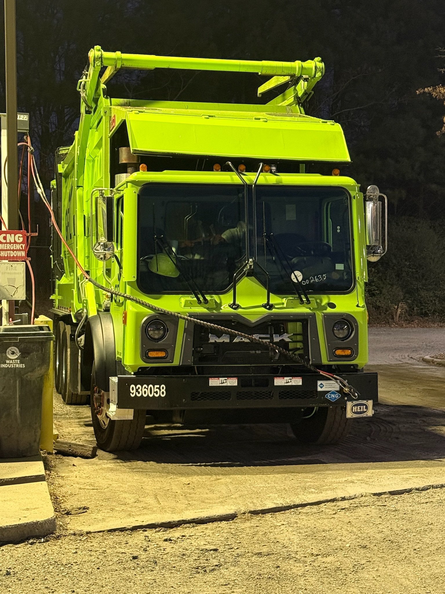 Bright yellow garbage truck with hydraulic lift mechanism parked on a street at night