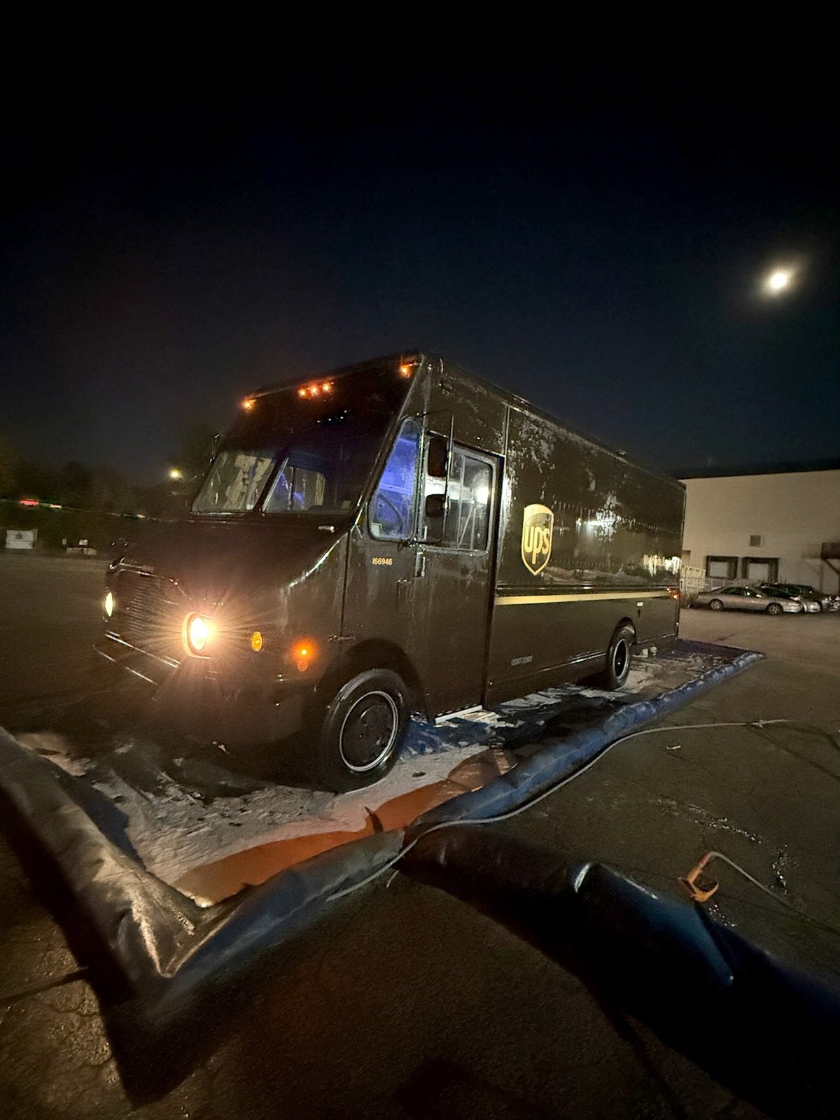 UPS delivery truck parked at night with illuminated headlights and running board in parking lot